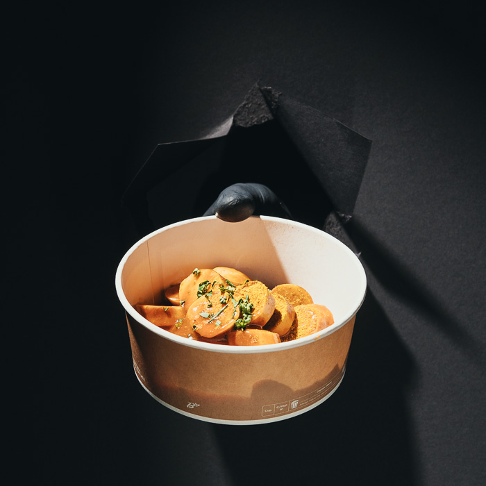 Currywurst in Scheiben mit Currysoße und Schnittlauch im Pappbecher