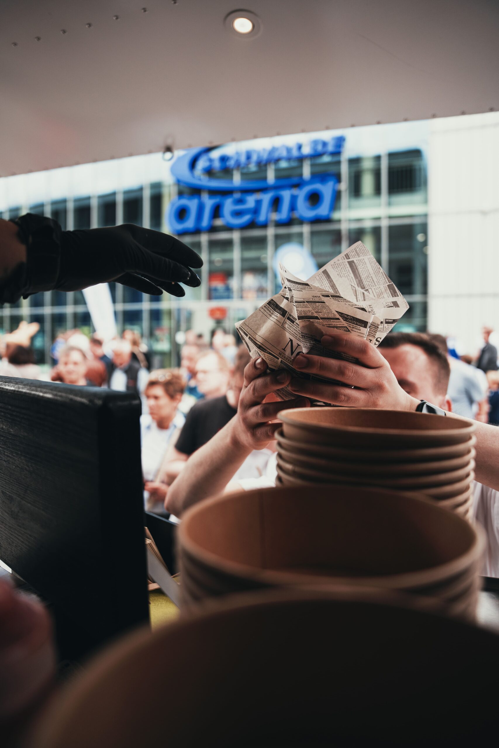 Burger und Bowls werden über die Theke gereicht, im Hintergrund Besucher vor der Schwalbe-Arena