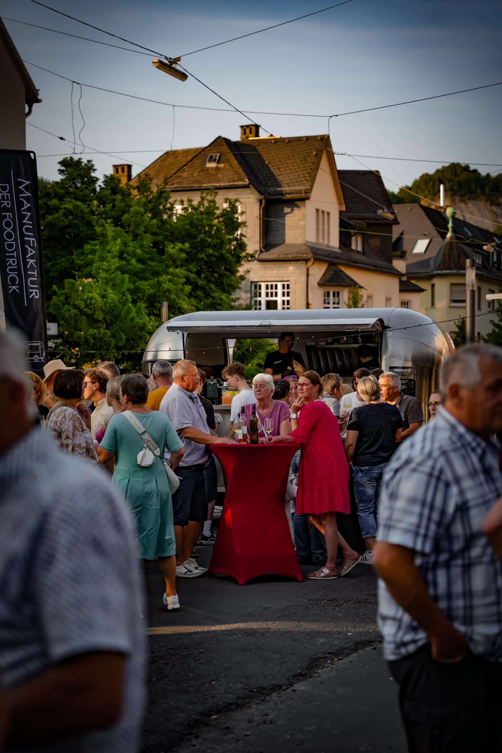 Viele Gäste an Stehtischen mit roten Hussen vor dem Foodtruck auf einem Straßenfest