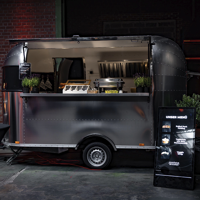 Airstream-Foodtruck mit geöffneter Theke und digitaler Menütafel in einer dunklen Halle