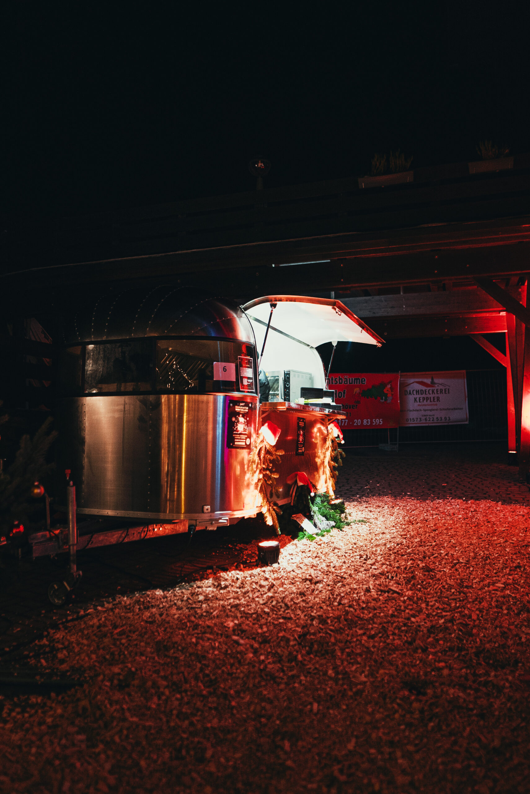 Airstream-Foodtruck bei Nacht unter einem Holzunterstand, rot angestrahlt