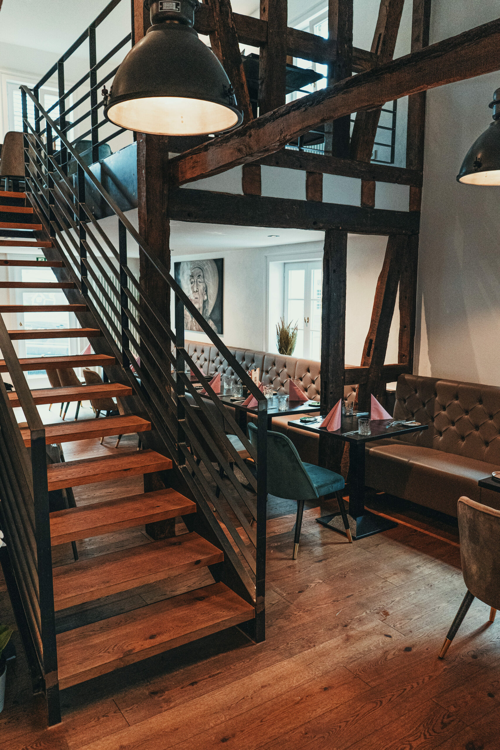 Fachwerk-Innenraum des Restaurants mit Holztreppe, Stahlgeländer und Industrieleuchten