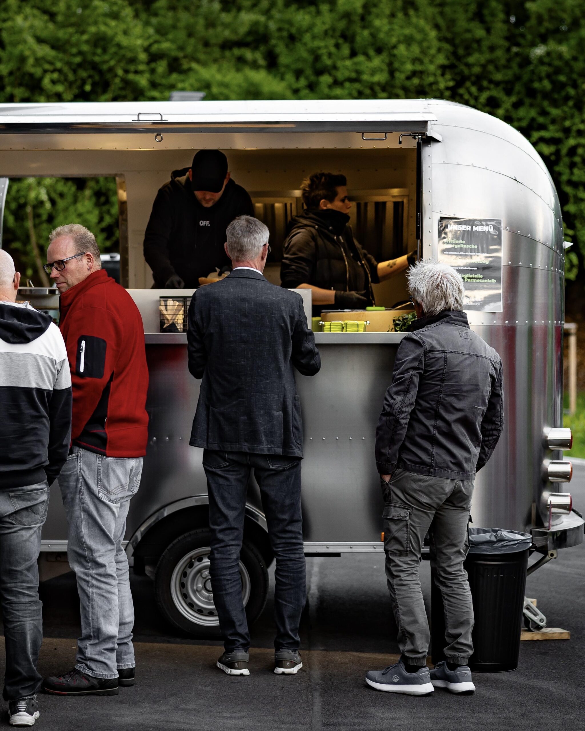 Gäste bestellen an der Theke des Foodtrucks, drinnen bereitet das Team das Essen zu